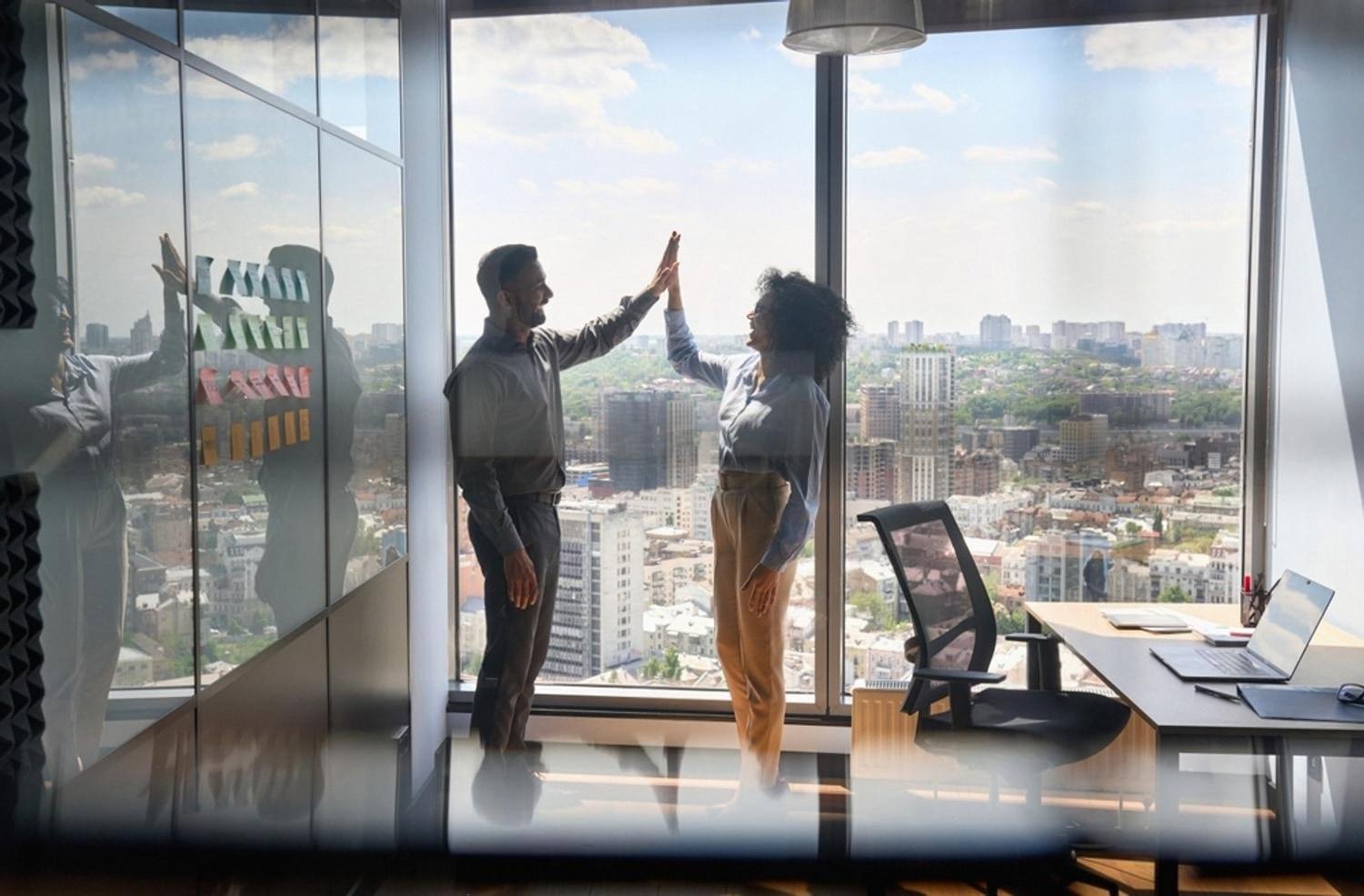 Two colleagues high-fiving in a modern office after a successful promotion decision